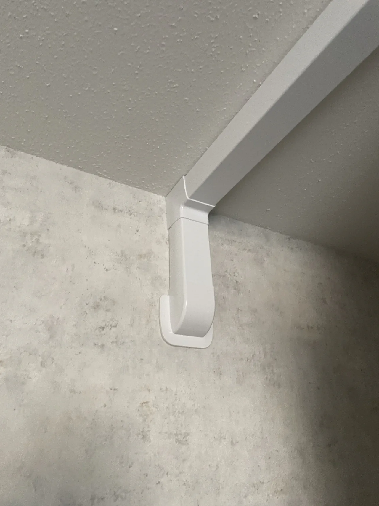Witte leidinggoot langs het plafond met een korte bocht naar beneden langs een grijze wand