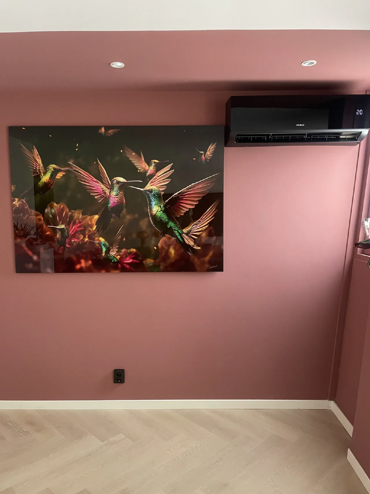 Zwarte Kaisai wandunit op een roze geschilderde wand naast een groot schilderij met kolibries, display toont 20 graden
